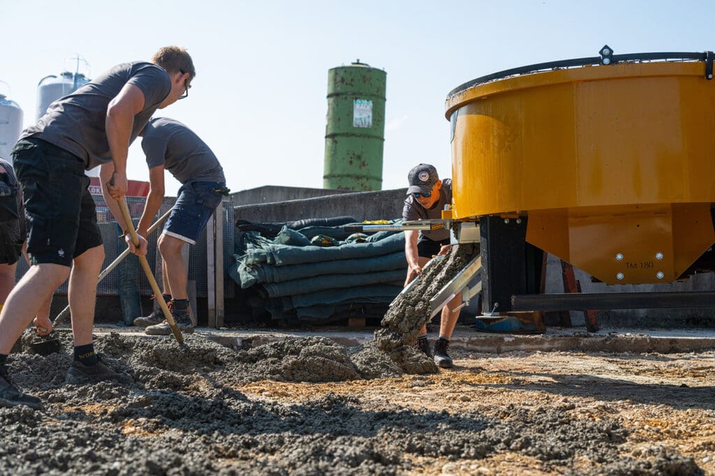 MAMMUT Zwangsmischer für Traktor TURBO MIX, Beton fließt aus schwenkbarer Rutsche und wird von Bauarbeiter verteilt